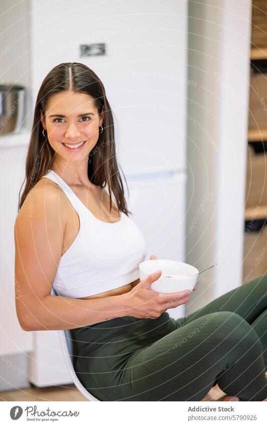 Smiling fitness woman at home eating healthy kitchen sportswear athletic meal cheerful bowl smiling lifestyle wellbeing nutrition indoor modern casual young