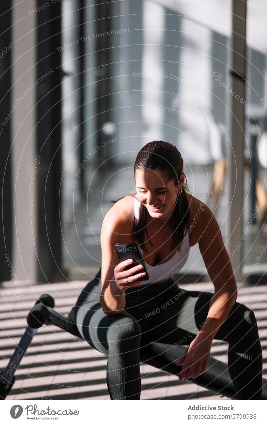Active woman using smartphone during workout at home sportswear fitness exercise break active lifestyle morning sun athleisure indoor health wellness technology