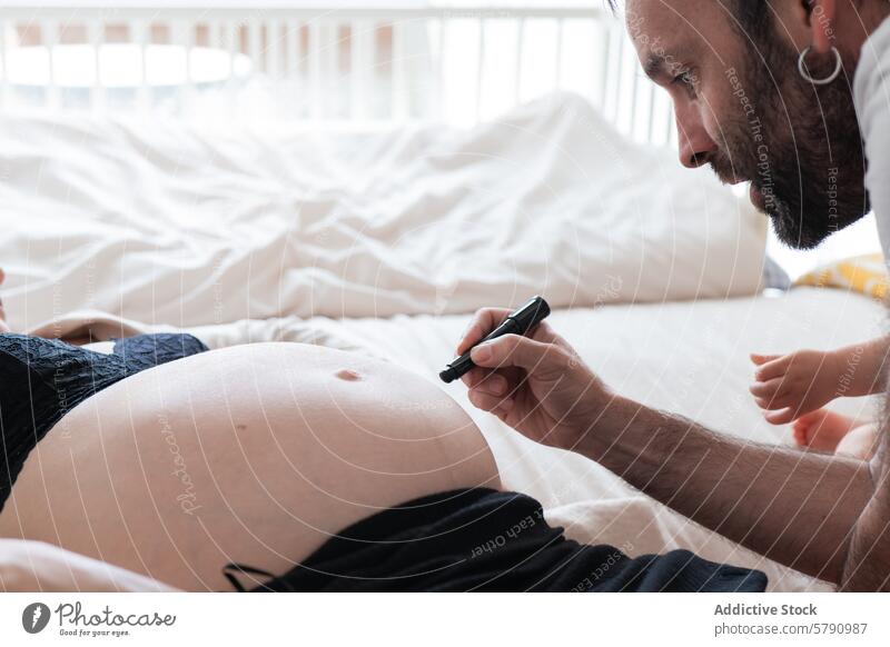Expecting father drawing on pregnant partners belly pregnancy bed tender moment expecting parent pen sketching prenatal maternity family love care bonding