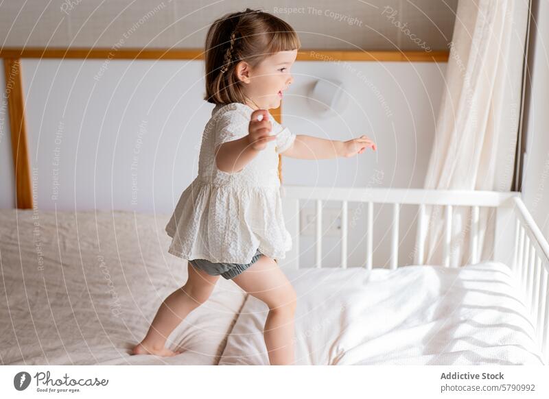 Little girl playing on a bed in a sunny room child bedroom sunlight cozy fun playful young innocence indoor daytime happy joy movement active toddler carefree