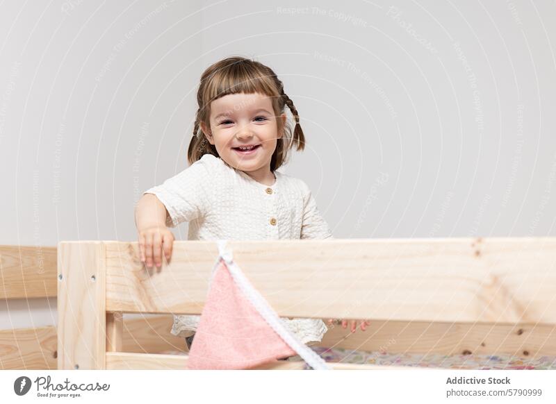 Happy toddler girl playing in a wooden bed smile happy child pigtails cheerful standing bedroom furniture blanket soft fabric indoors home comfort cozy
