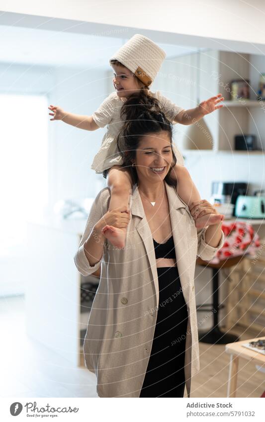 Joyful pregnant mother giving young daughter piggyback ride at home family joy laughter happiness kitchen woman child girl smile bonding playful indoors care