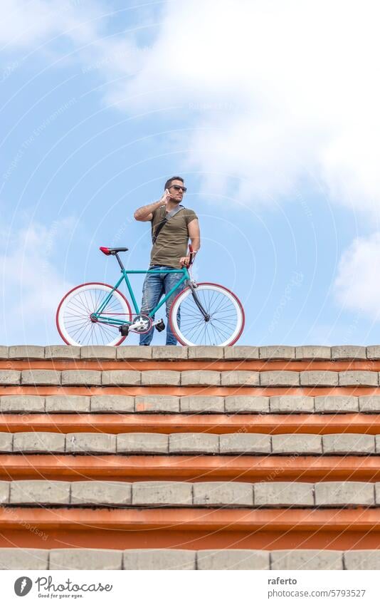 Man with bike on rooftop calls bicycle calling phone sky urban lifestyle connectivity confident mobile communication leisure outdoor city casual modern