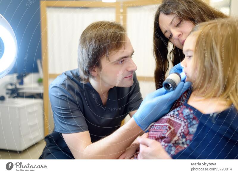 A caring doctor checks moles on the skin of a small child. A dermatologist looks at a rash on the neck of a girl using a dermatoscope. Baby at a pediatrician appointment