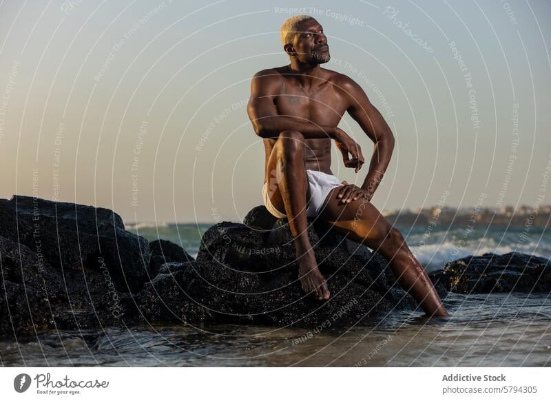 African American Male Model Posing on Beach Rocks at Dusk model male african american beach dusk rocks ocean serene posing thought ethnic black water