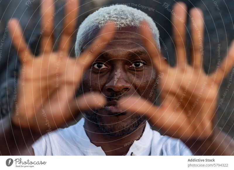 A compelling close-up portrait of an African American man with striking white hair, gazing through his outstretched fingers gaze hands spread face intense