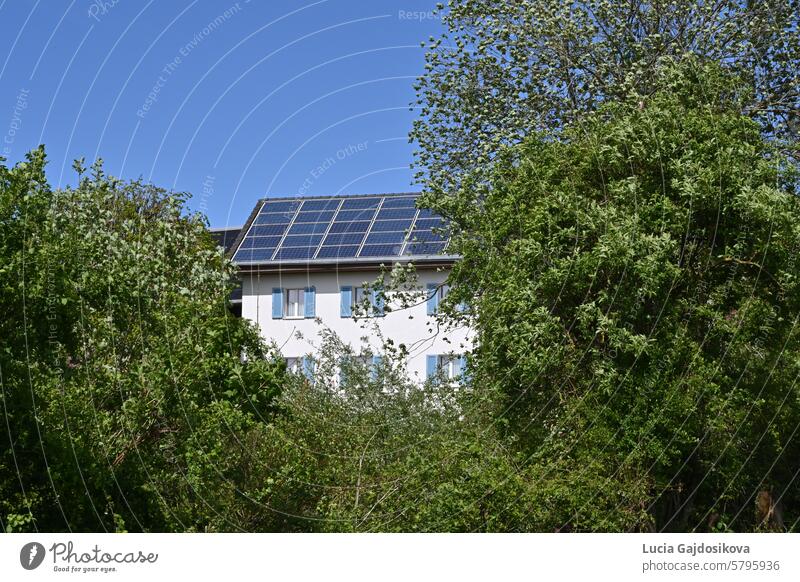 Installation of solar or photovoltaic panels on the roof of family house observed during sunny day in a Swiss village. There are trees and bushes around the house.