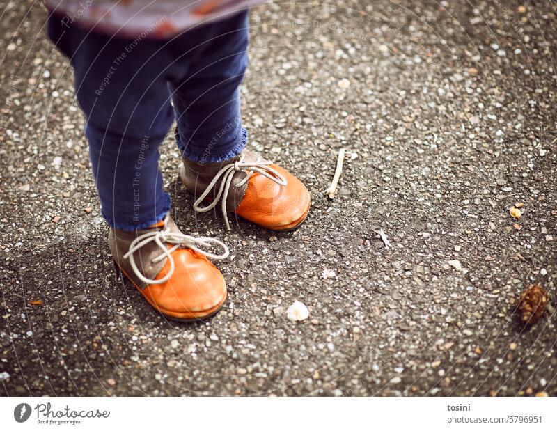 Toddler stands on asphalt with orange shoes Child Infancy Footwear Tying your shoes Asphalt Stand learn to walk Walking Childrens shoe shoelaces Legs