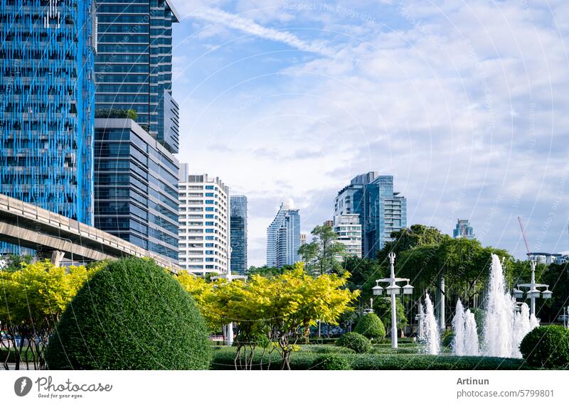 A city with tall office buildings and a central fountain. Sustainable cityscape surrounded by trees and bushes. Sustainable city design. Urban environment. Lush city park. Inside a green cityscape.