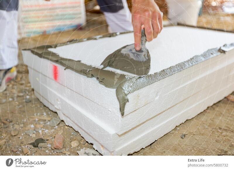 Worker applies the glue to thermal isolation material, styrofoam with spatula Adhesive Affix Apply Applying Attach Building Site Cement Civil Engineering