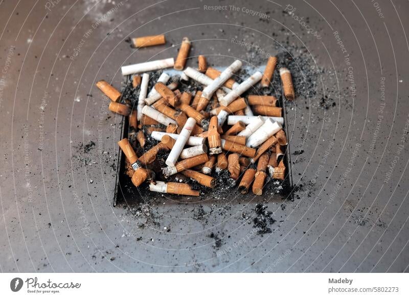 Overfilled ashtray on a metal tray with butts and filter cigarettes in a passageway in the old town of the trade fair city of Leipzig in the Free State of Saxony
