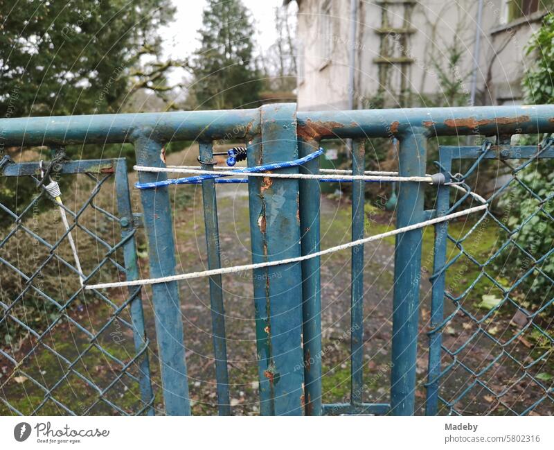 Tensioning strap on a rusty old farm gate in front of a neglected property with a vacant old house in Wettenberg Krofdorf-Gleiberg near Gießen in Hesse
