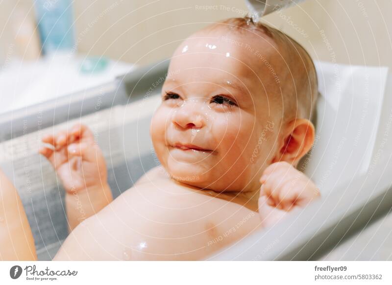 Portrait of a nine month old baby taking a bath with water running trough his face bathtub portrait toddler boy male shower caucasian months old sitting
