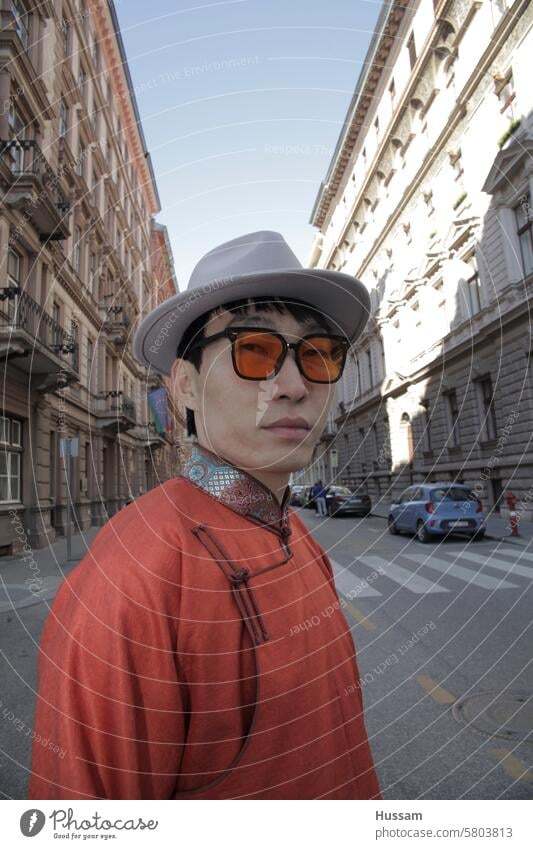 photo of asian person looking at the camera wearing dress of modern Mongolian pattern with hat and vintage sunglasses in European  street fashionista city man