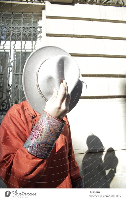 a photo of ananymous person holding hat covering his face with shadow reflecting on old buidling travel fashion man city building architecture creative street