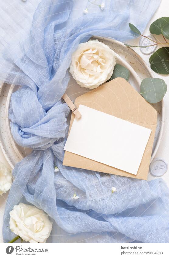 Card and envelope near blue tulle fabric and cream roses top view copy space, wedding mockup card romantic flowers knot white silk spring mothers day light blue