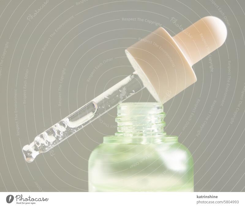 Drop falls from a pipette resting on a bottle filled with green serum agains gray, macro liquid close-up Natural organic gel oil cosmetic product woman beauty