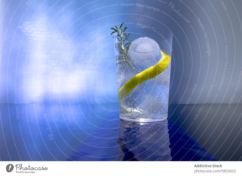 Gin tonic cocktail with ice and lemon on blue gin drink beverage alcohol refreshing sphere peel garnish glass background bubbly fizzy cold bar mixology spirit