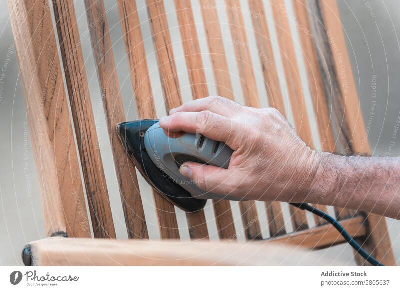 Close-up of Man Sanding a Wooden Chair hand electric sander wooden chair sanding smoothing surface varnishing work manual labor furniture restoration