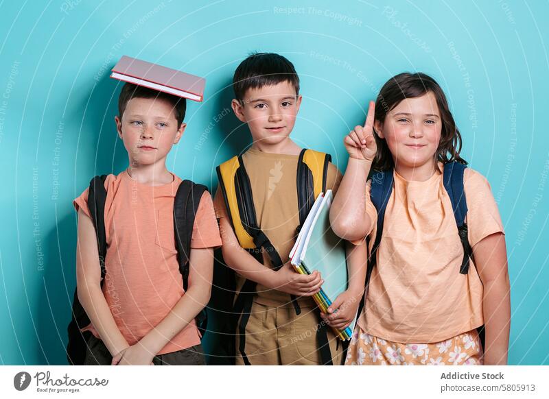 Three school kids with backpacks and books boys girl blue backdrop education smiling looking at camera standing casual clothing student learning childhood