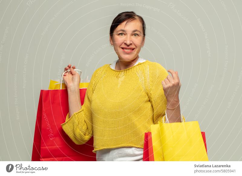 Portrait of a happy adult woman with gift bags on a gray background.shopper. Woman person Bags Fashion Sale Attractive Beauty & Beauty Shopping Load Lifestyle