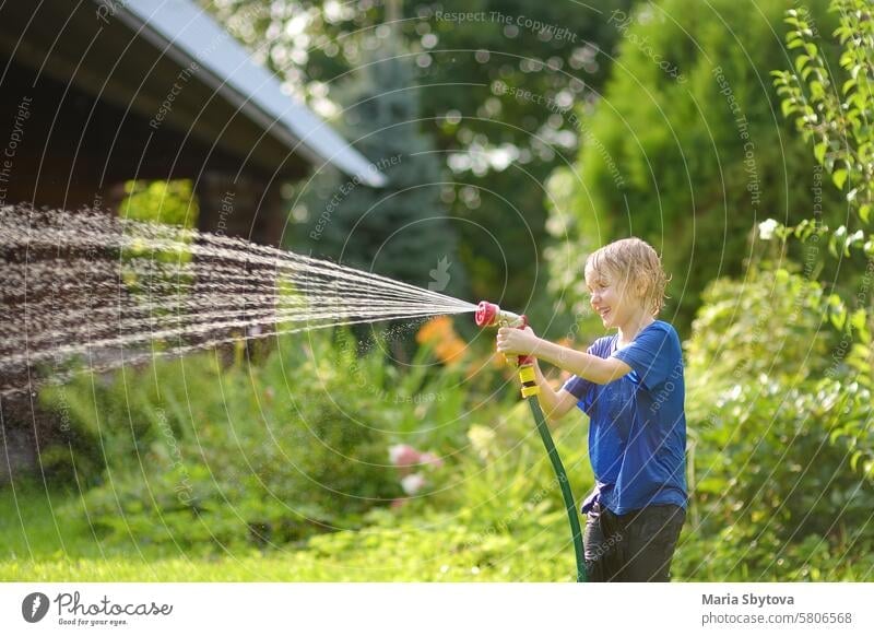 Funny little boy playing with garden hose in sunny backyard. Preschooler child having fun with spray of water. Summer vacation in the village for kids. family