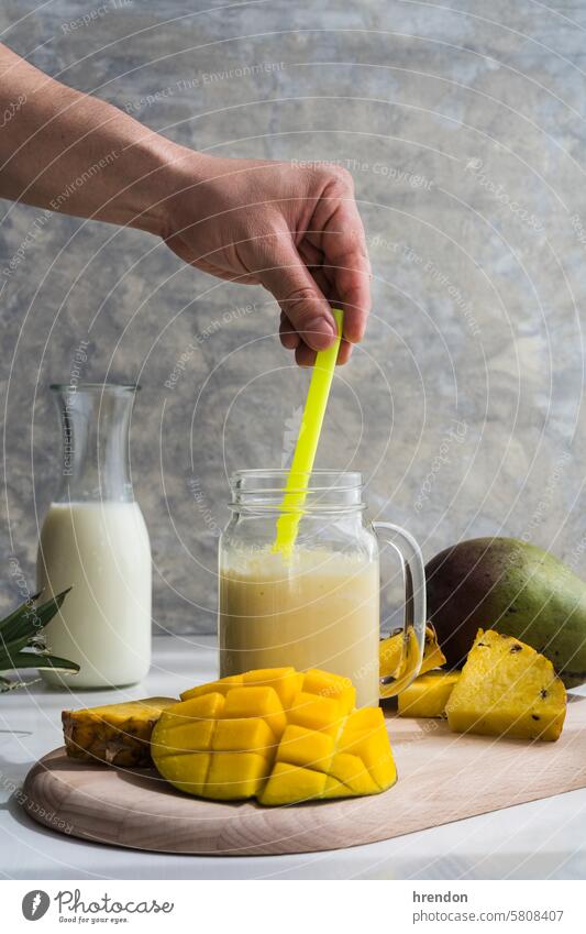 hand stirring an mango and pineapple smoothie with a straw drink food fruit organic healthy breakfast juice glass diet cocktail beverage blended fresh juicy