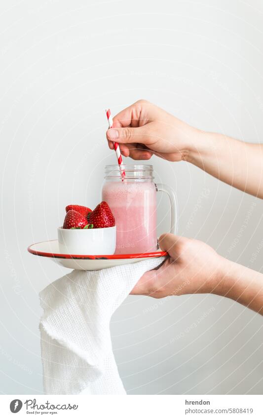 a hand holding a plate with a jar of strawberry smoothie on a white background drink food fruit organic healthy breakfast juice glass diet cocktail beverage