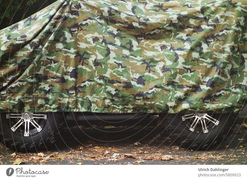 All-terrain vehicle under camouflage cover with the wheels partially protruding. Camouflage Hiding place War military Hide