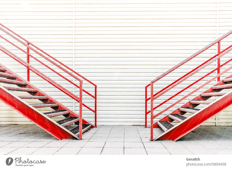 two red metal stairs on the background of a wall finished with siding Two ways alternative architecture building choice choise downstairs equal house iron left
