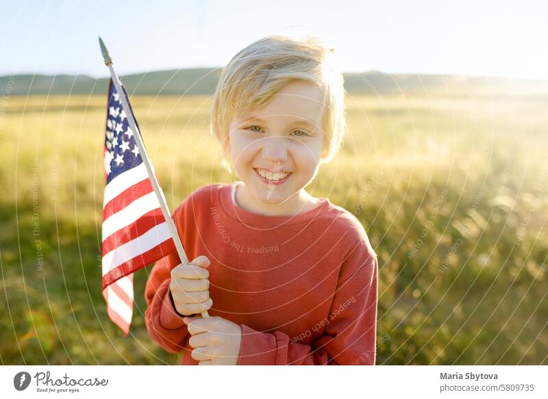 Cute little boy celebrating of July, 4 Independence Day of USA at sunny summer sunset. Child running with american flag of United States on wheat field. child