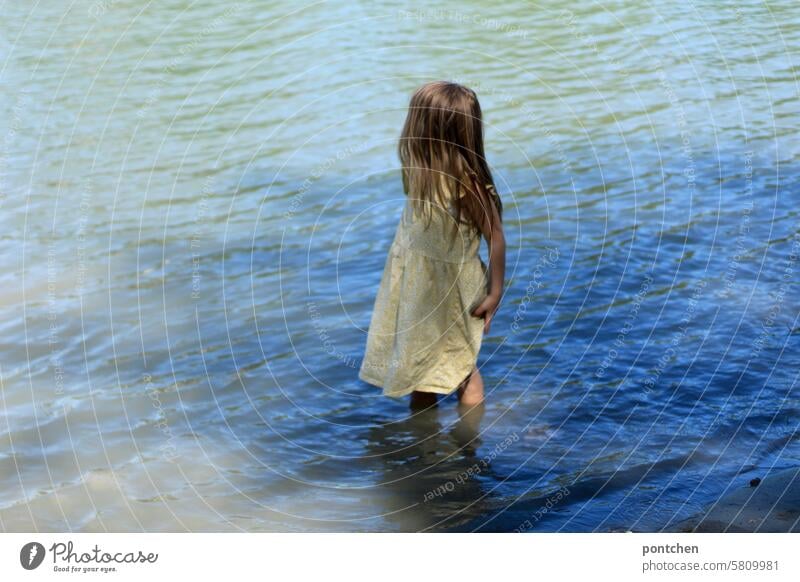 a child in a dress stands ankle-deep in water. refreshment Child Water Refreshment Girl Dress long hairs Blue River Inn Exterior shot Summer Nature