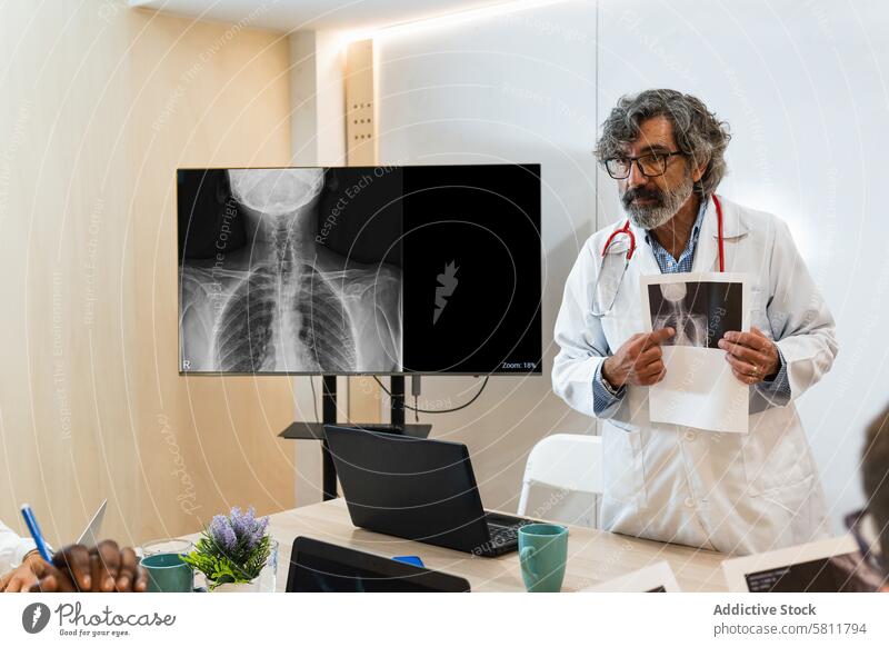Senior doctor discussing x ray with colleagues in hospital medic coworker image professional clinic medical office senior elderly aged explain uniform talk