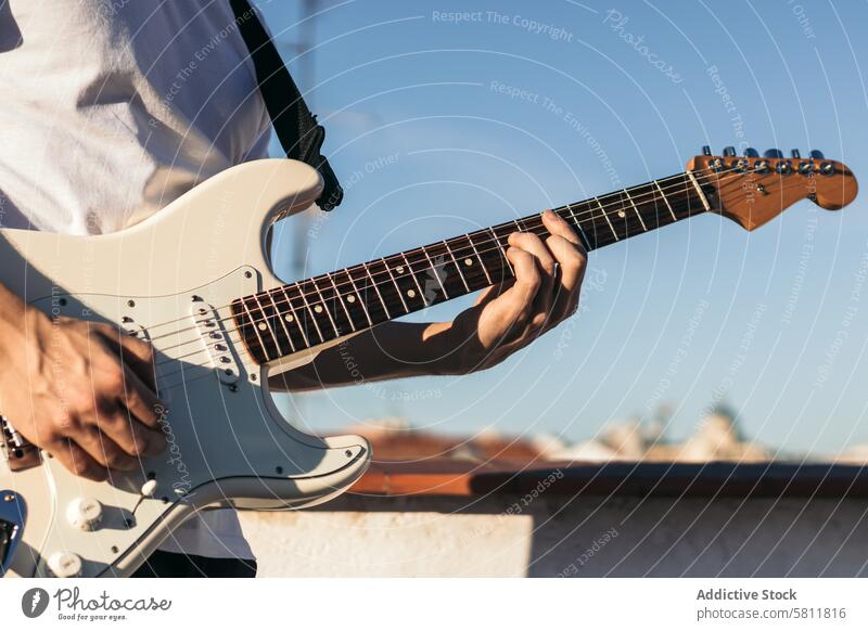 man playing electric guitar on a rooftop instrument musical guitarist musician sound guy black acoustic performer clouds sky player male concert band rock stage