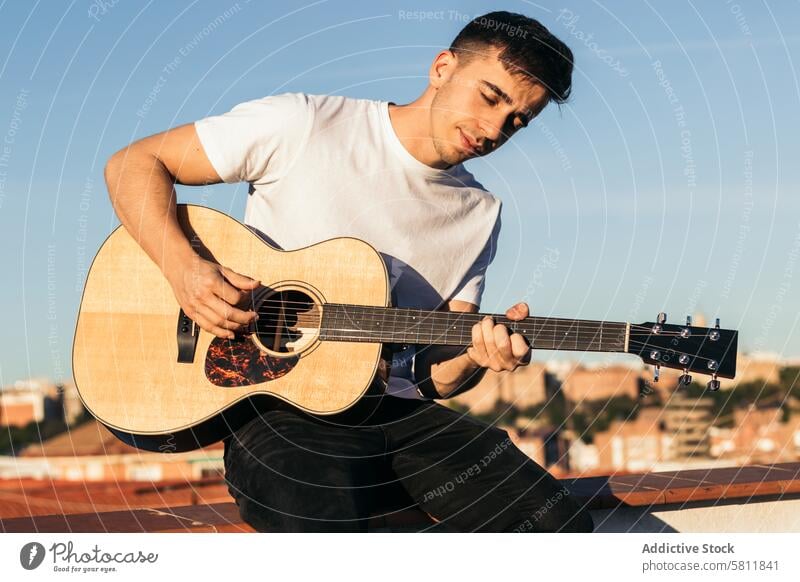 young man sitting playing acoustic guitar on a rooftop musician guitarist male person instrument player musical casual rock people caucasian handsome song