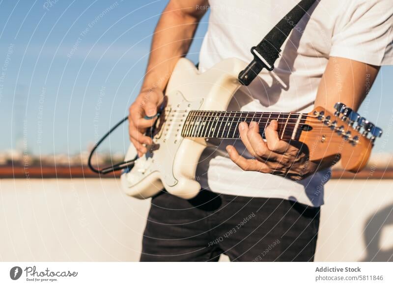 man playing electric guitar on a rooftop. close-up instrument musical guitarist musician sound guy black acoustic performer studio clouds sky player male