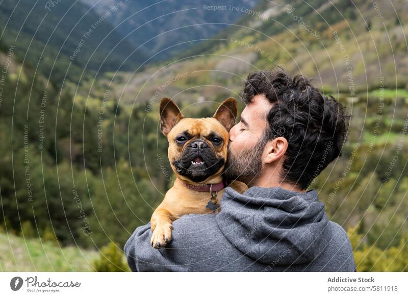 Happy traveling man kissing cute dog in highlands mountain together embrace traveler hiker male pyrenees french bulldog rock freedom pet animal journey