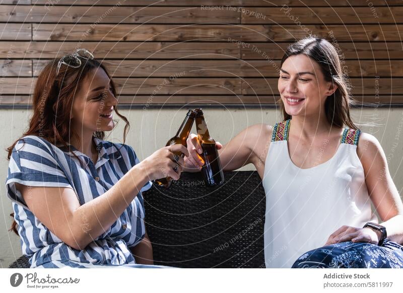 Cheerful girlfriends with beer spending weekend on sofa cheers interact cheerful spend time lifestyle portrait women smile chill alcohol drink bottle beverage
