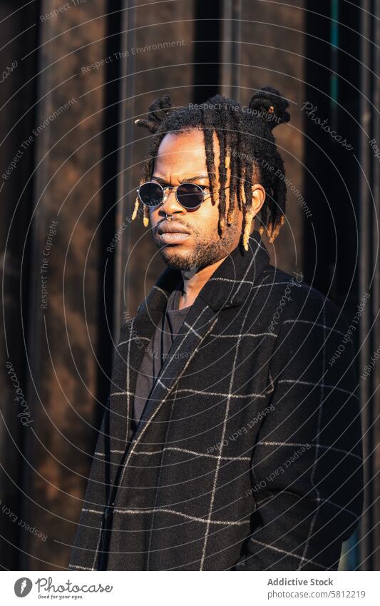 Stylish black man with dreadlocks in buns street style cool urban modern coat sunglasses hairstyle frown informal trendy culture accessory independent casual