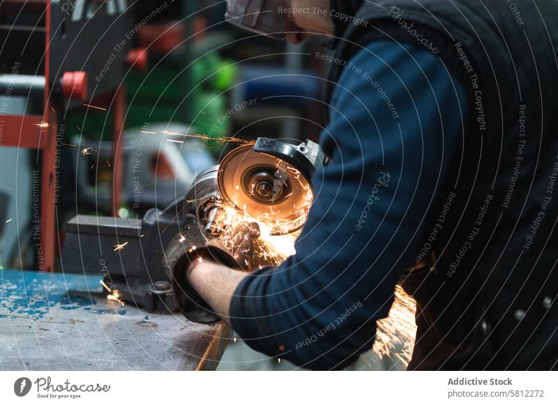 Attentive repairman cutting metal with electric grinder in workshop mechanic metalwork spark skill job equipment male adult casual goggles tool process