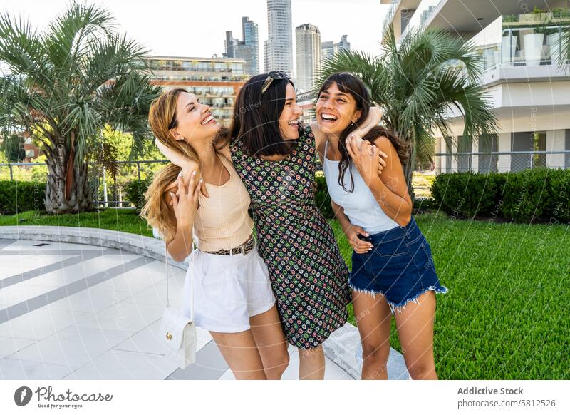 Portrait of three friends embracing together while laughing adult attractive beautiful blonde brunette casual caucasian city enjoyment fashionable female
