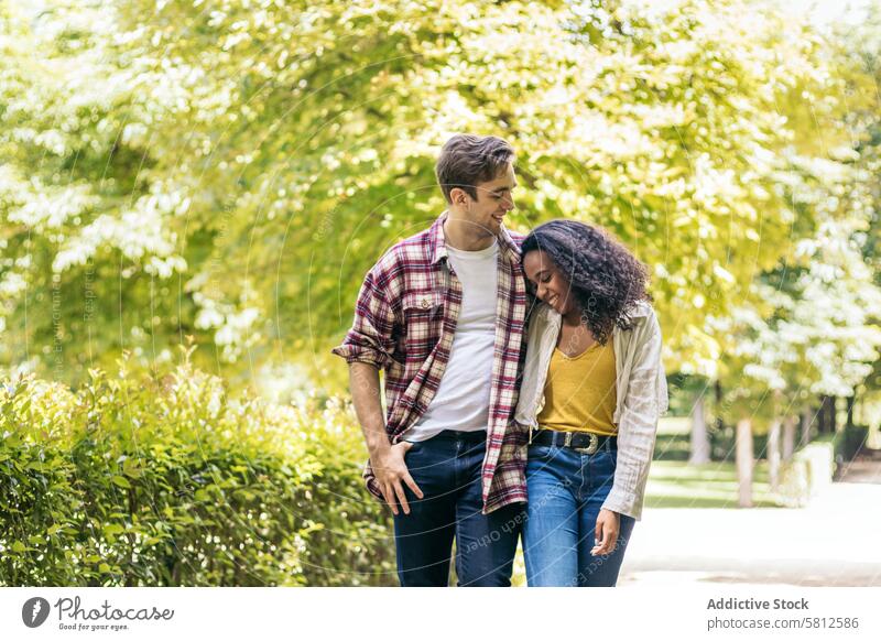 Happy multiracial couple taking a walk in the park outdoors smartphone happy lifestyle together young people multiethnic fun boyfriend relationship caucasian