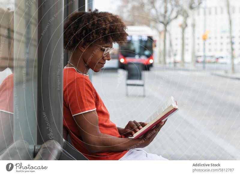 Calm young black male reading novel at bus stop man book street city relax trendy millennial wait urban african american man black man ethnic afro casual