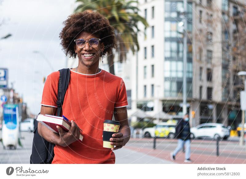 Cheerful young black guy walking on street with takeaway coffee and textbooks in hands man smile student city happy to go cheerful male casual eyeglasses