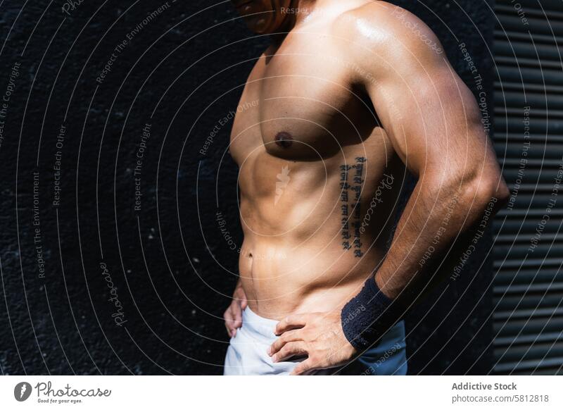 Anonymous positive shirtless Hispanic sportsman near wall training healthy lifestyle wellness fitness muscular naked torso street male sportswear sporty