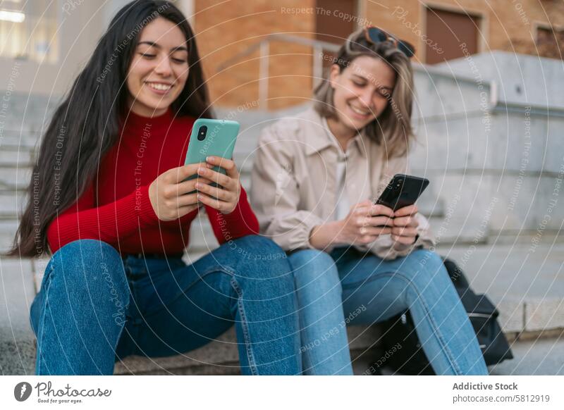 two student girls sitting on the stairs watching the mobile young friends phone female internet students people couple smartphone happy caucasian university