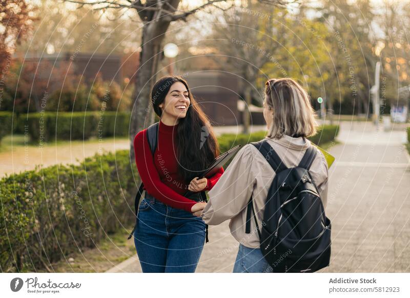 Back view of two student girls talking and laughing woman happy side together friendship girlfriend young people female couple person love teen college