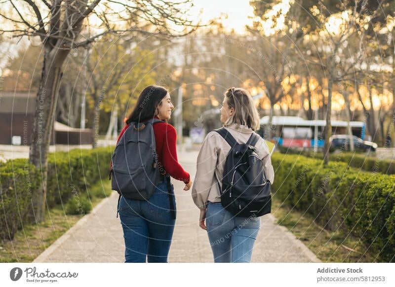 Back view of two student girls walking and talking in campus friendship together outside young happy relationship park lifestyle female woman fashion