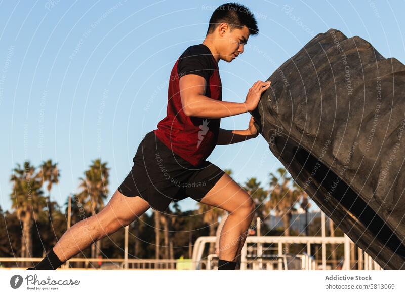 Strong man doing tire flip exercise sportsman workout strong asian ethnic fitness training sporty athlete lifestyle wellness wellbeing male vitality effort
