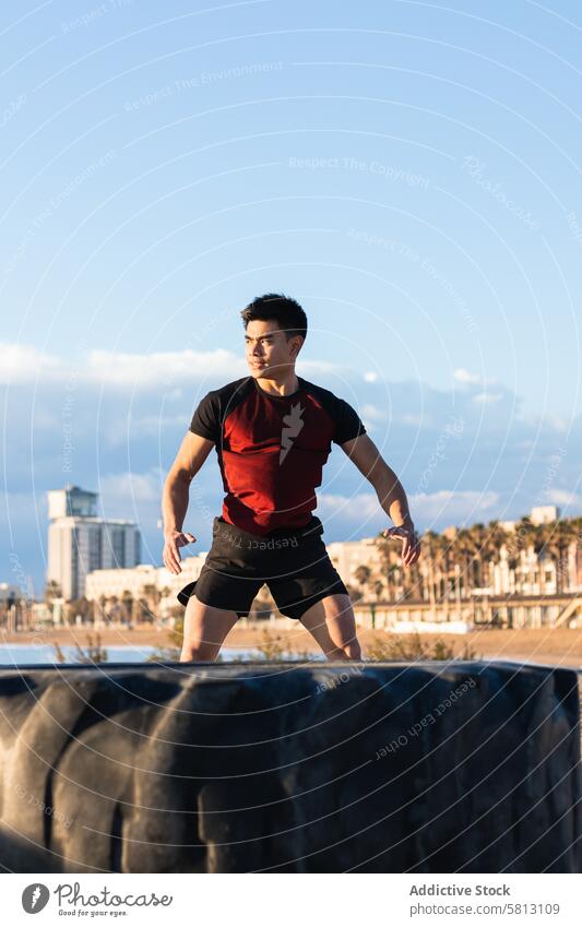 Strong ethnic sportsman jumping near tire during fitness workout training exercise strong energy sporty warm up lifestyle athlete wellness wellbeing male
